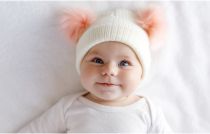 Cute baby wearing warm, white hat with pink bobbles